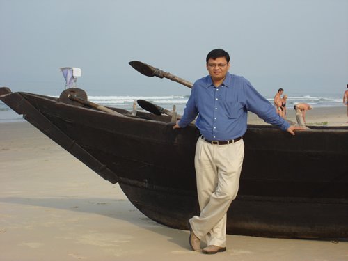 A man in a blue shirt standing by a boat on the beach.